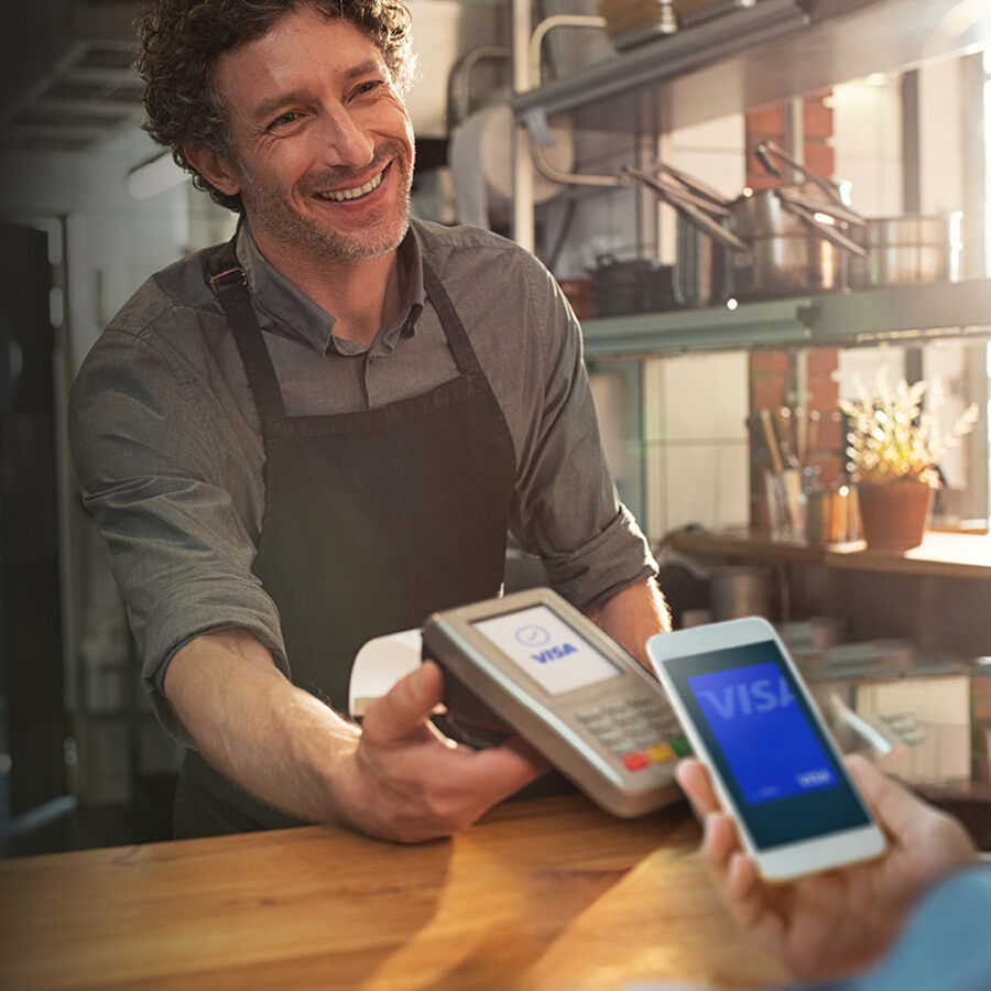 man smiling holding POS device with Visa logo. Phone tapping device with Visa card on screen